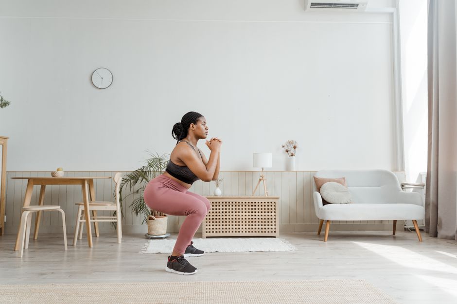 Mulher fazendo agachamento em casa, sobre um tapete de exercícios