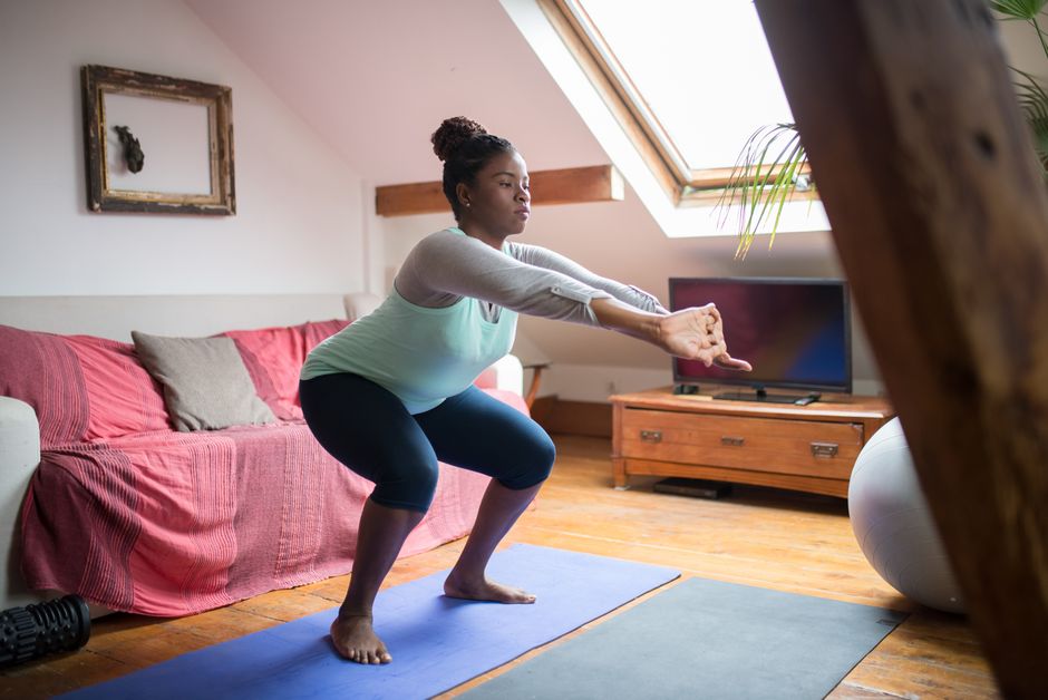 Mulher fazendo agachamento em casa, sobre um tapete de yoga